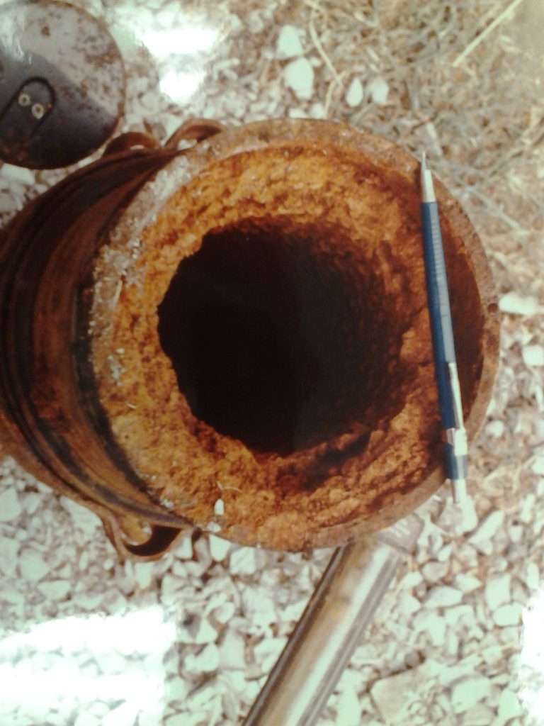 Iron encrustation in a well casing, with a pencil for scale. The well diameter is similar to pencil length, and the iron buildup creates a ring approximately 1-inch wide inside the well casing.