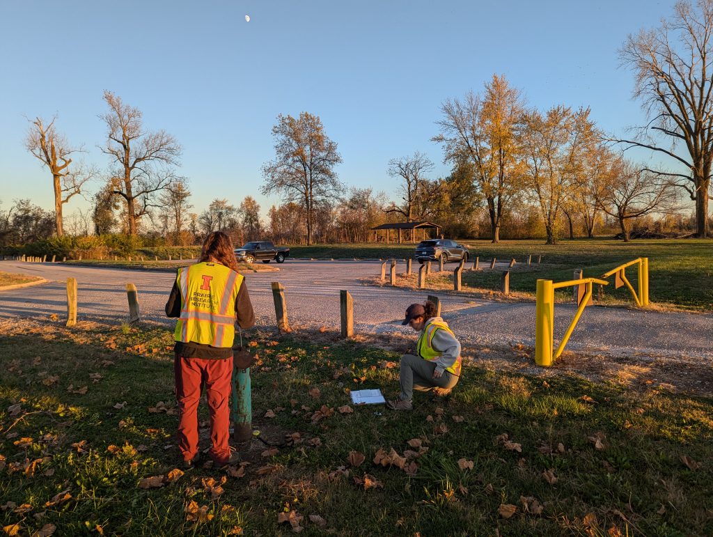 Two CH4DS researchers measuring groundwater levels at wells located near a parking lot at a State Park.