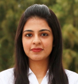 Portrait of Garvita Allabadi looking at the camera. She has long dark hair styled back from her face and is wearing a white collared shirt. The background is softly blurred greenery, creating a natural outdoor setting.