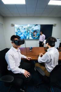 Students interact with virtual reality visor while what they see is shown on a screen
