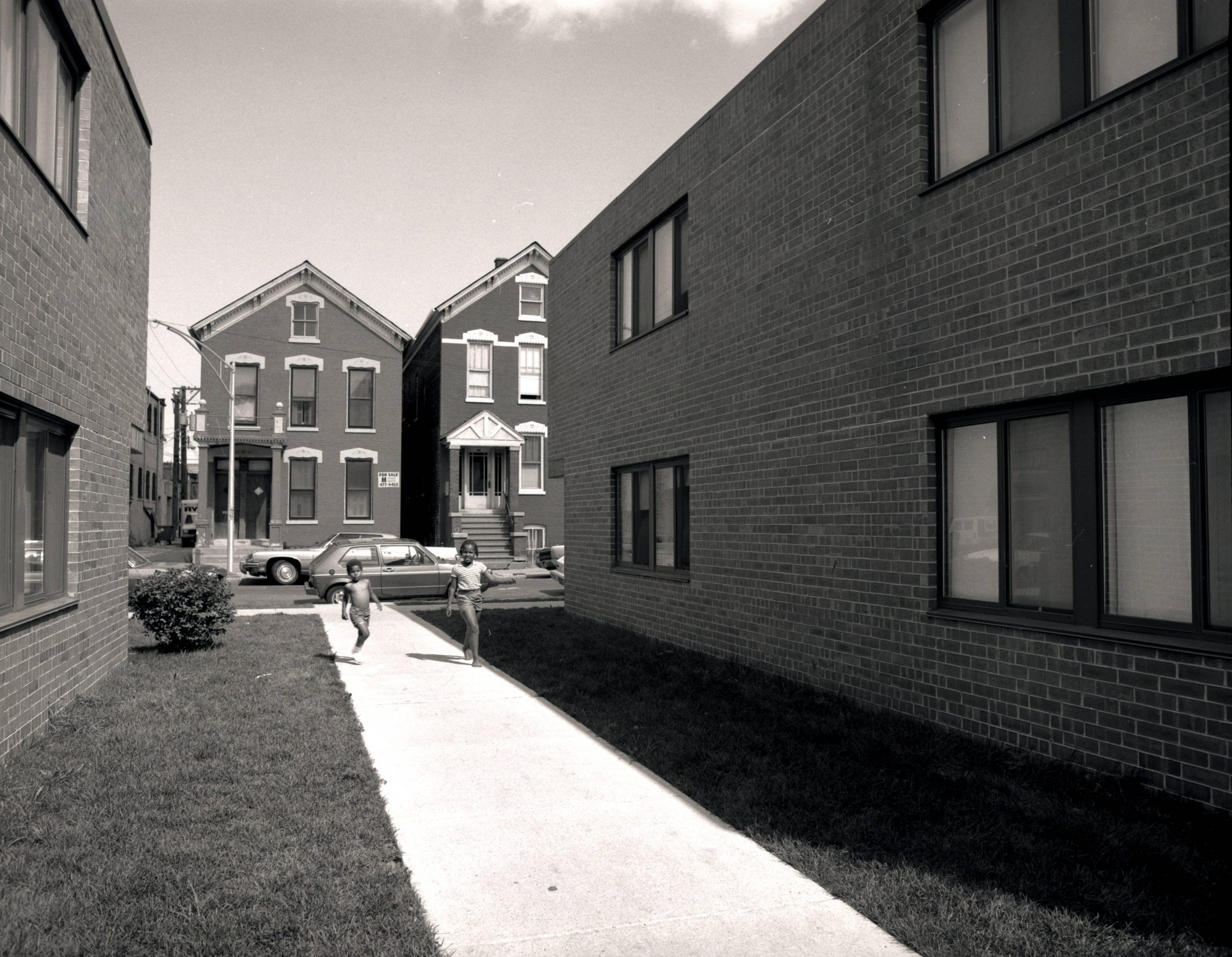 Two children are walking down the sidewalk between two new buildings.