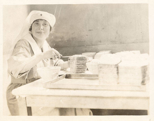 A nurse prepares a tall tower of sandwiches at a table. Stacks of ready sandwiches are on the table as well.