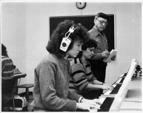 Students in a class wear headphones while practicing on electronic piano keyboards.