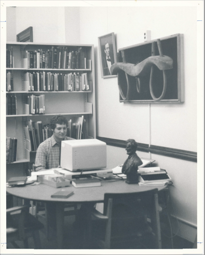 Student sits at a computer under the ox yoke and beside a bust of Lincoln.