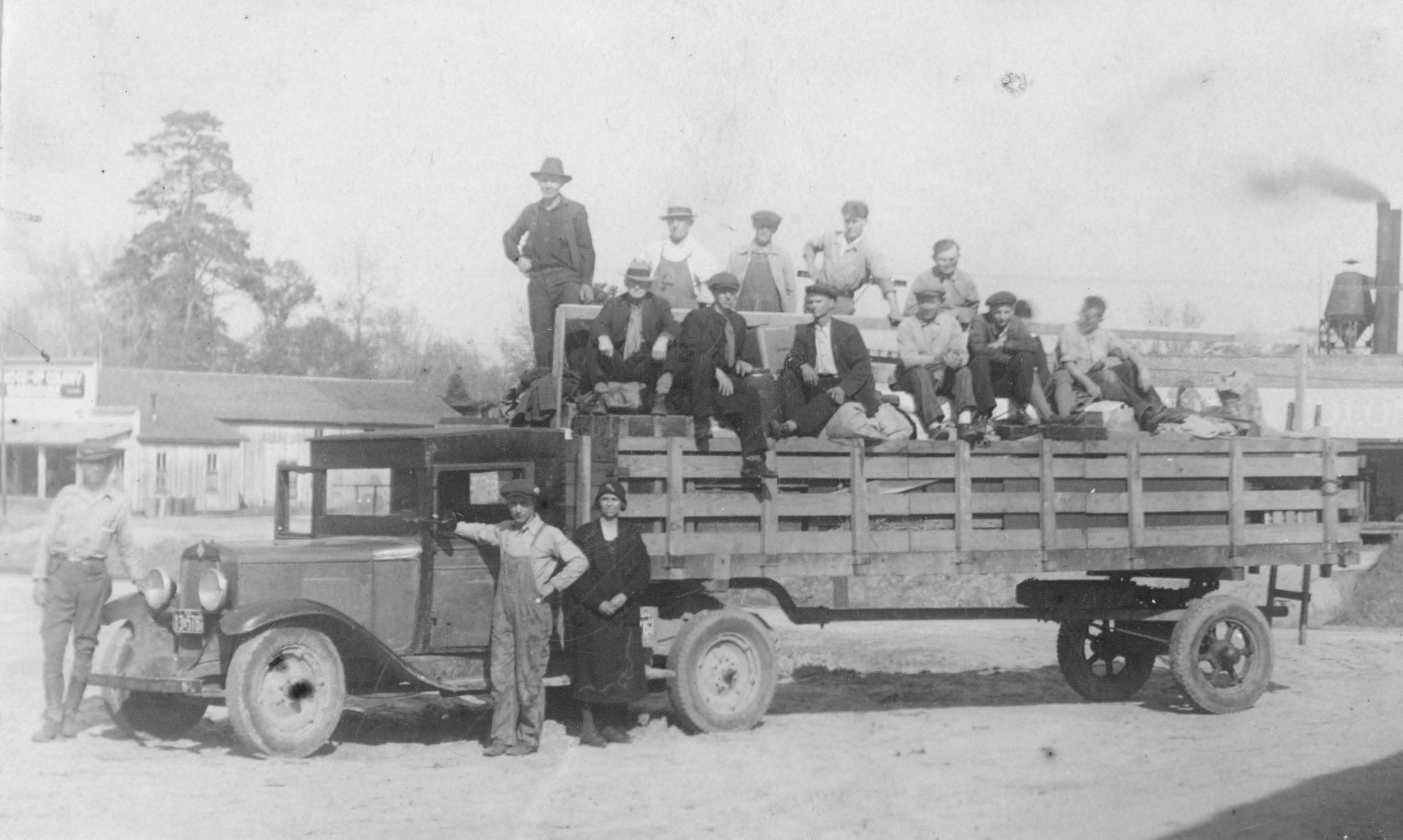 Grayscaled photograph of a group of people standing on bed of truck circa 1933