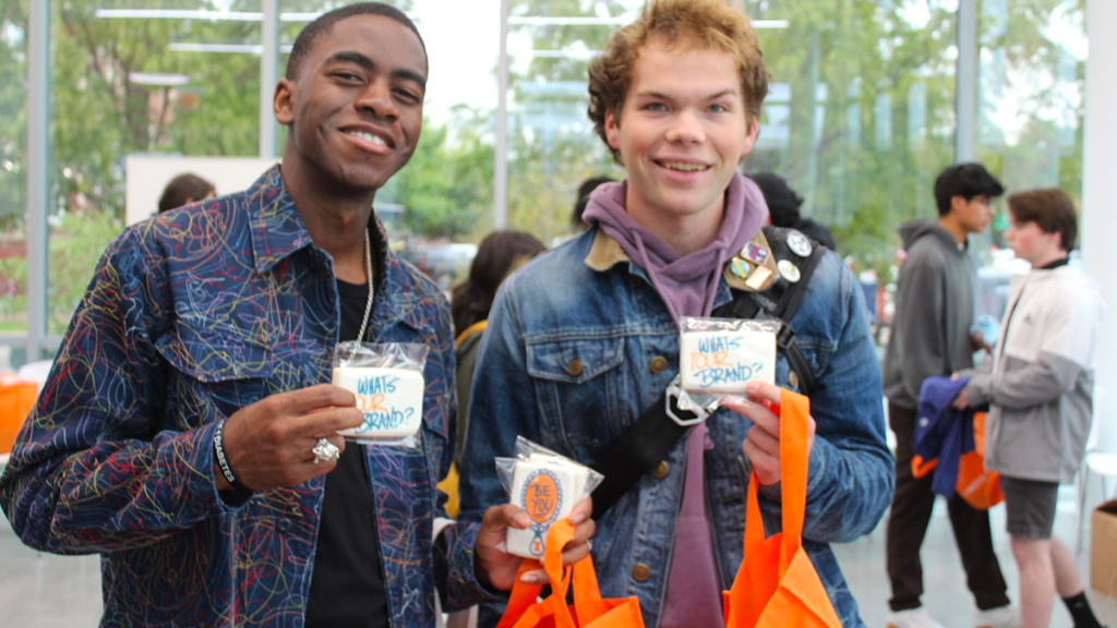 two advertising students showing of advertising-themed cookies at the annual ADV + You event. 
