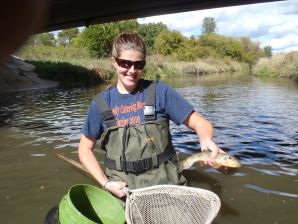 Samantha Jaworski stands in a stream, holding a fish and net