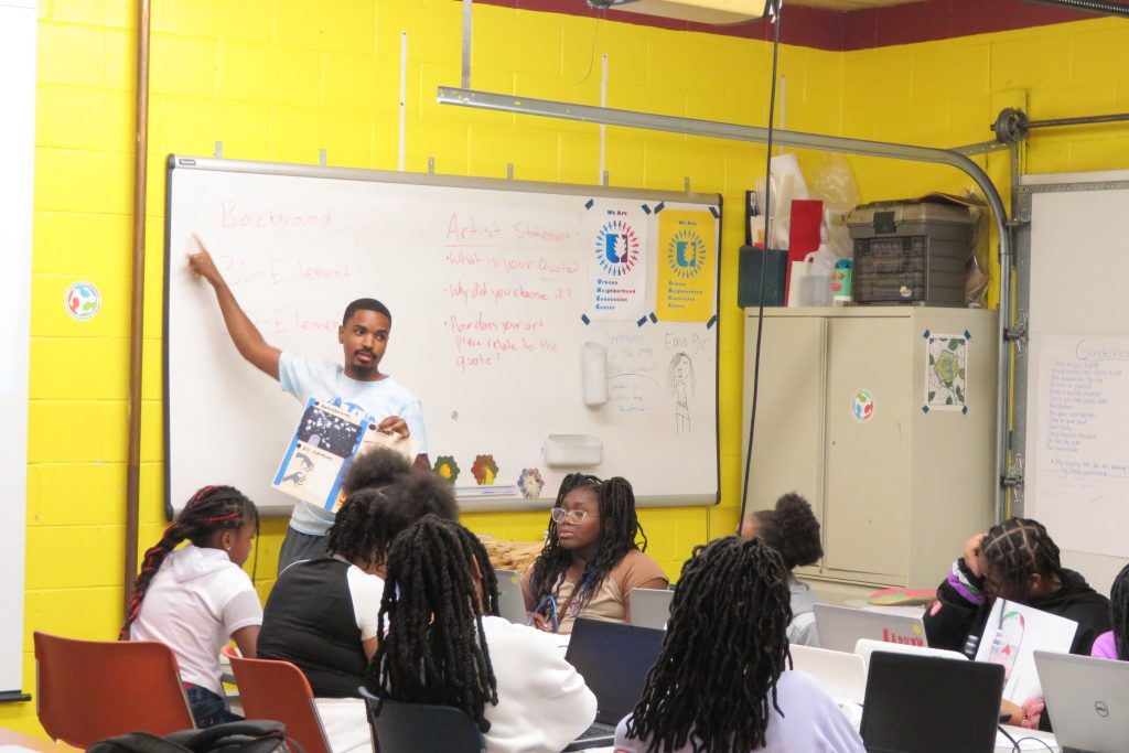 Champaign Urbana Community Fab Lab staff member leading a session, pointing to a whiteboard in front of session attendees.