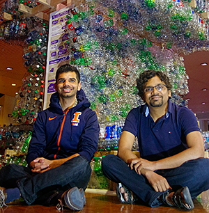 Two men sitting in front of waste sculpture