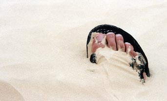 foot buried in sand, with sandaled toes jutting out