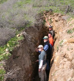 four people stand in a deep ditch to examine the soil