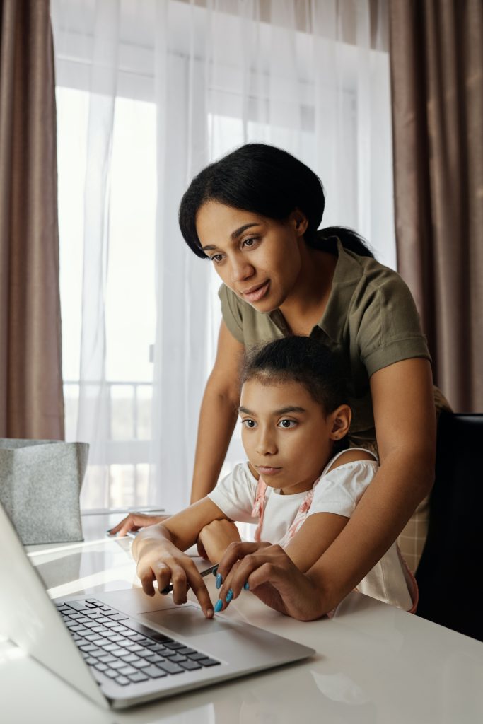 Photo of two people in front of a computer, with one older person guiding the hand of the younger person. 