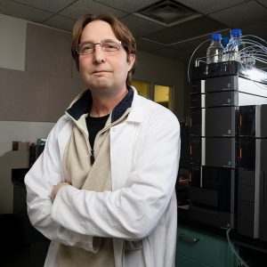 John Scott wearing a lab coat in a dark moody ISTC lab.