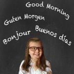 Cute little girl in elementary school thinking of all the languages she wants to learn and speak. Blackboard background. Multilingual and bilingual concept.