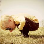 A young child is bending down looking in the grass, investigating something with a magnifying glass. Vintage style color.