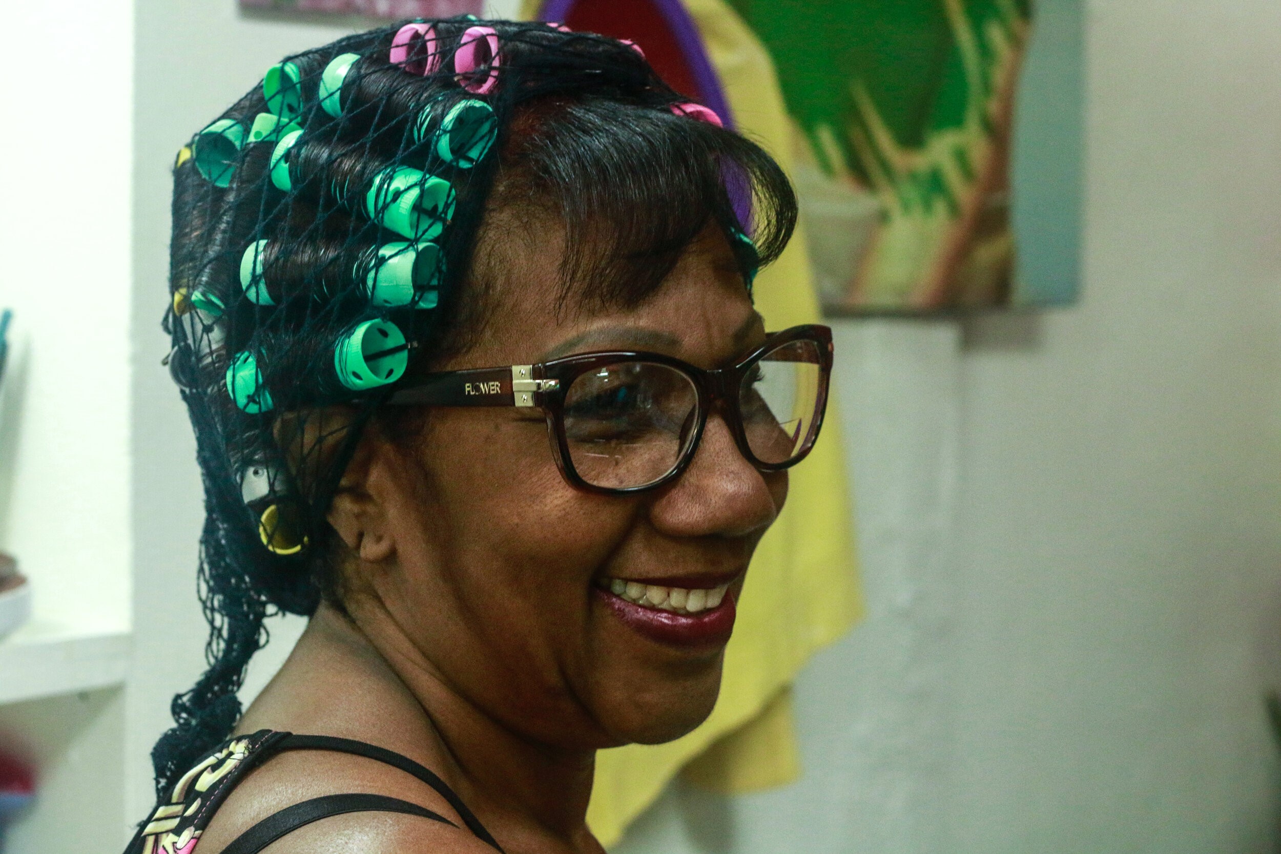 Image from Dominican-Puerto Rican artist Ojos Nebulosos’ photo essay “Quisqueyanas: Ferminas Salón.” Features a smiling woman in glasses with curlers in her hair.