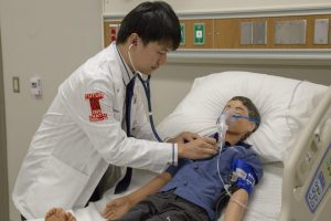 Student Andrew Chang listens to Derek's lungs after the respiratory therapist started the nebulizer.