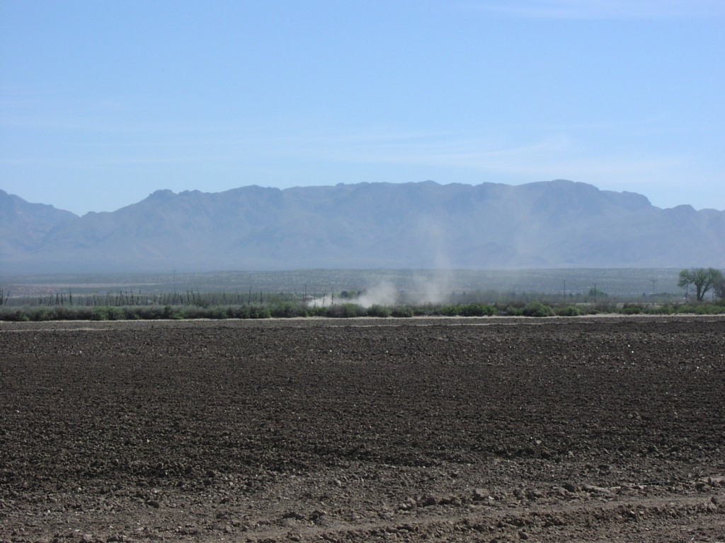 A disced field with smoke or dust in the background