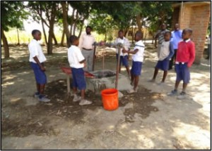 Uniformed African school children filling a bucket at a well.