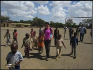 A Caucasian woman speaking with African school children in a playground.