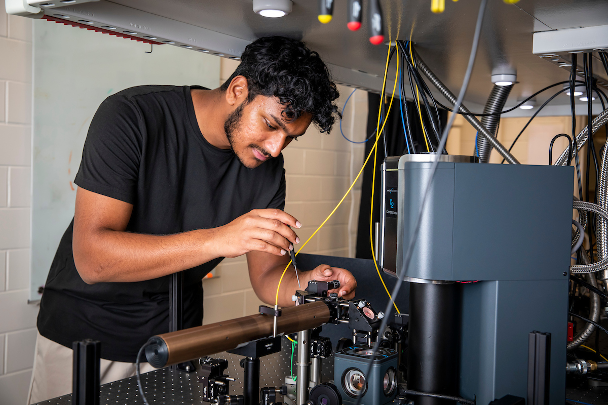 An Indian student wearing a dark T-shirt uses a screwdriver to adjust a research device.